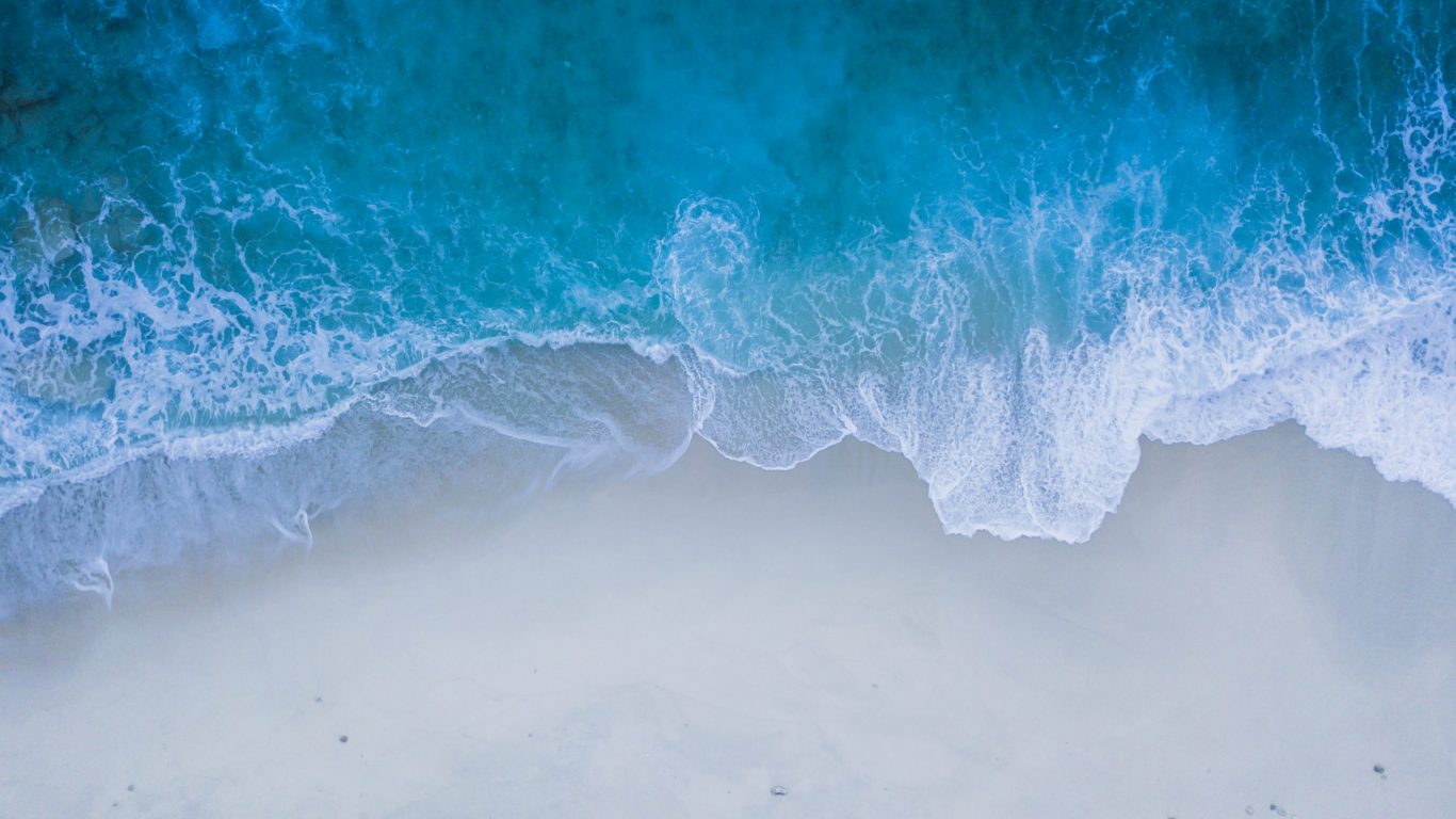 Foto van een zandstrand waarop golven breken op slowcialmedia waarbij je gefocust kunt werken
